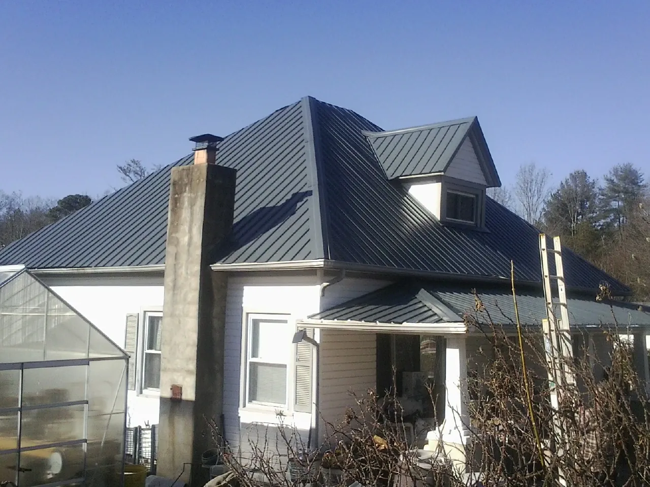 Dark blue standing seam metal roof on a white farmhouse with dormer — Slate & Tile Roof Repair by Roofing Brothers in La Vista