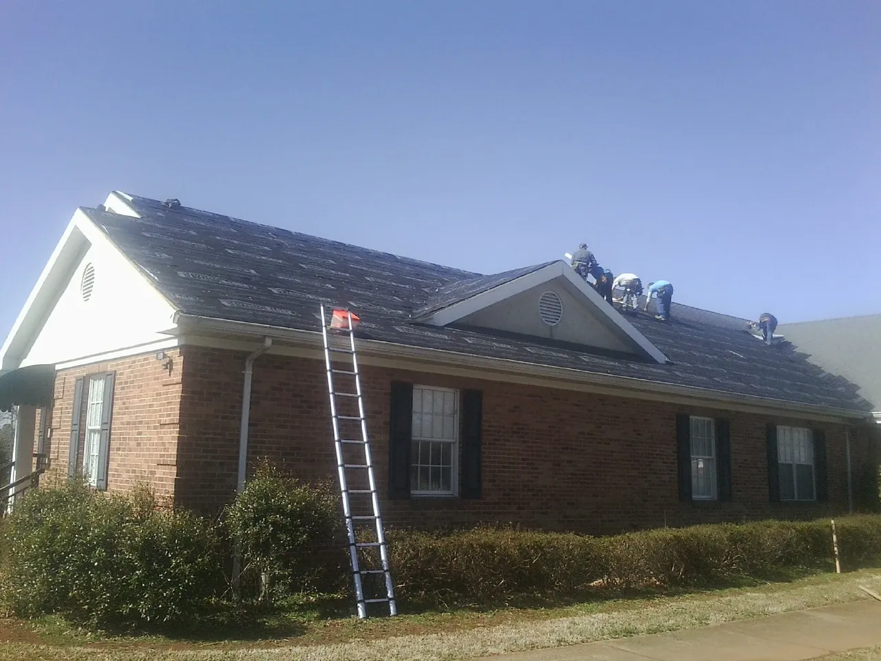 Crew tearing shingles off a brick ranch roof with a ladder set — Emergency Roof Repair work by our crew in La Vista
