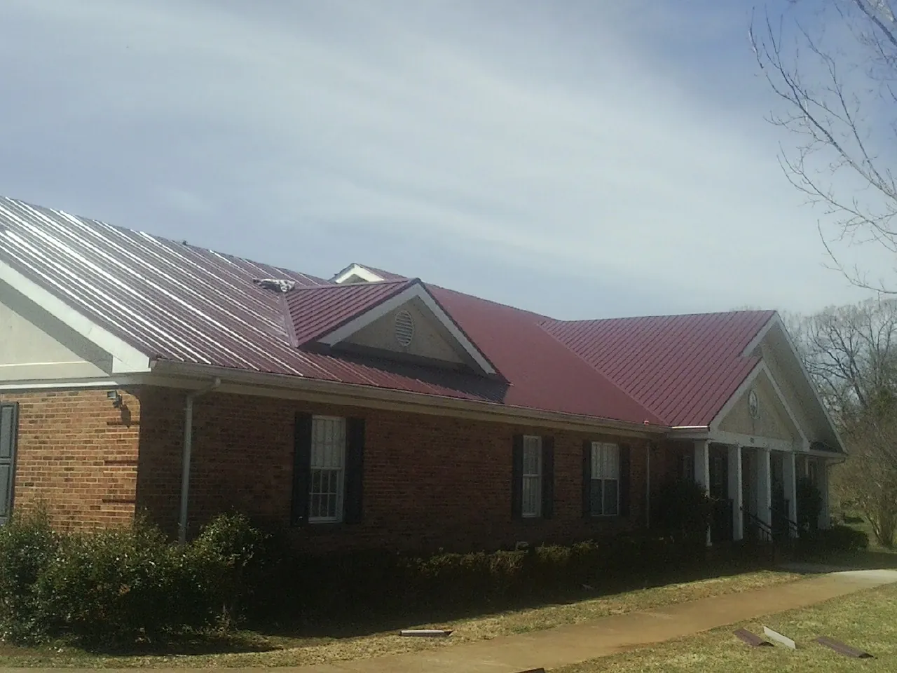 Red metal roof with gabled entries on a long brick building, from a Hail Damage Roof Repair job in La Vista