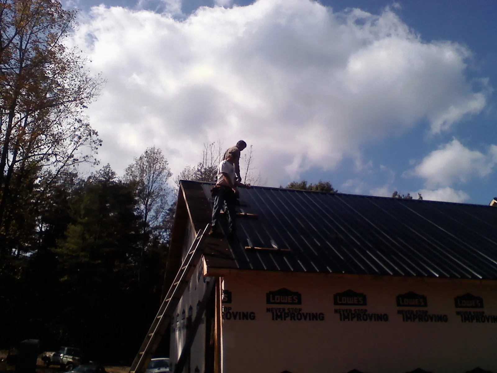 Roofer fastening dark metal panels high against a cloudy sky, from a Roof Inspection job in La Vista