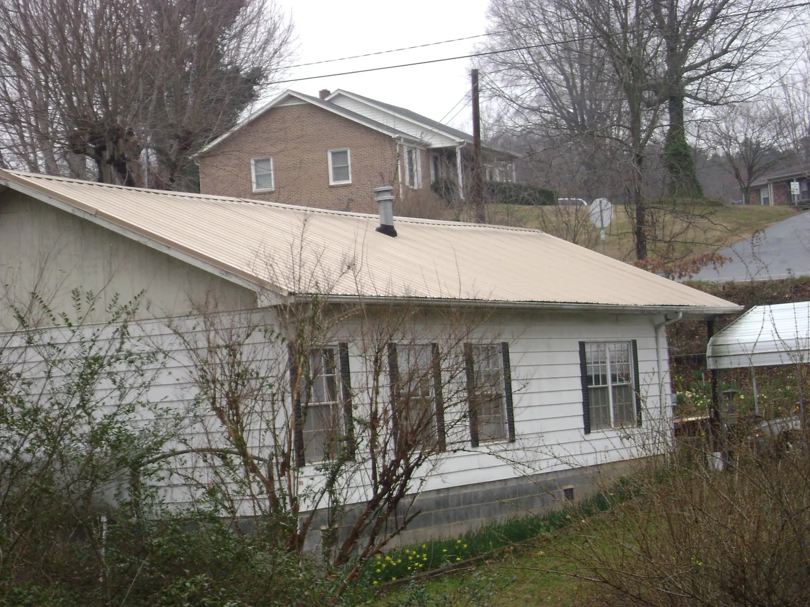 Tan metal roof on a white sided house set into a hillside — Commercial Roofing by Roofing Brothers in La Vista