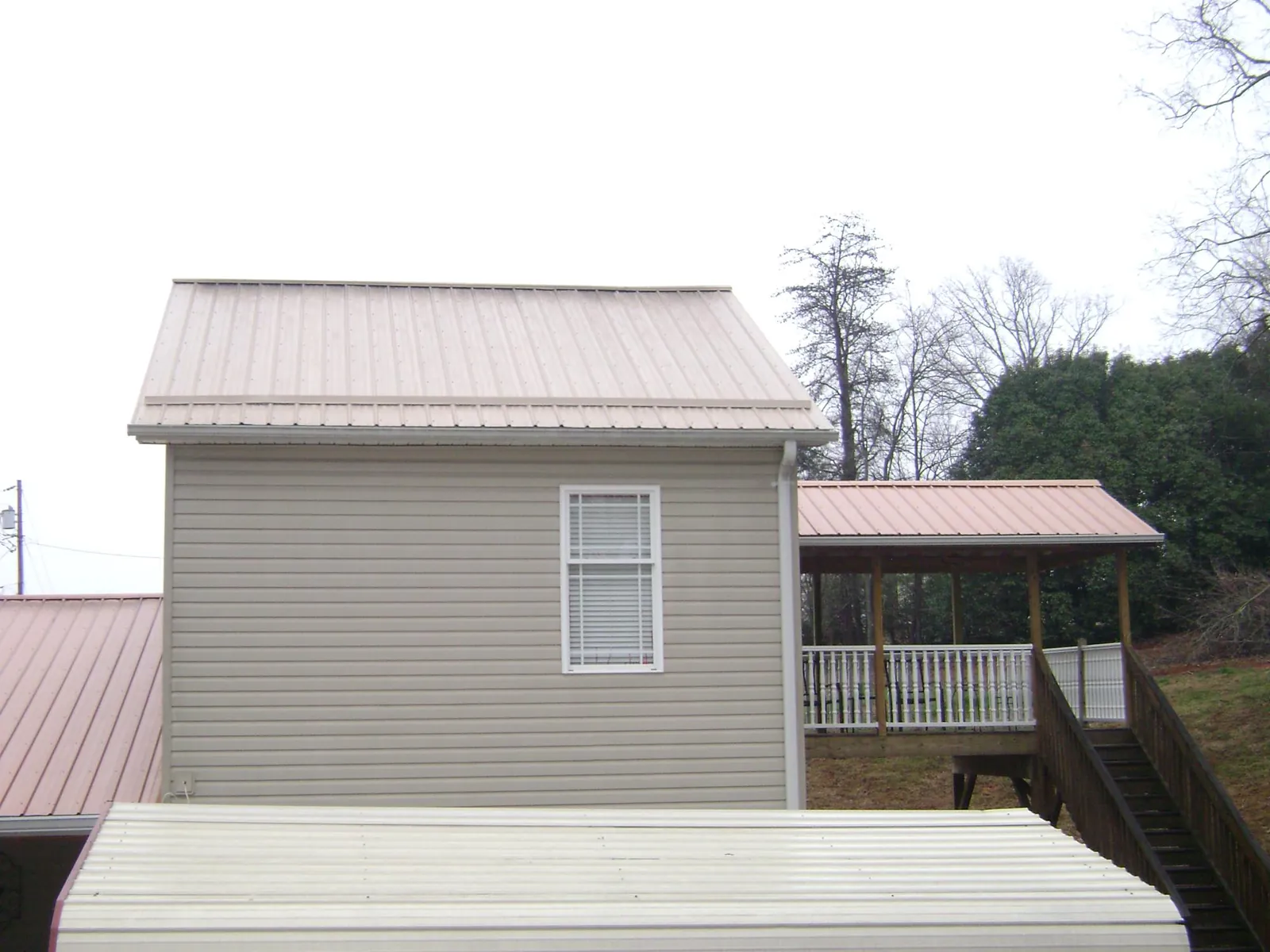 Tan metal roofs on a two story addition and attached porch, from a Roof Replacement job in La Vista